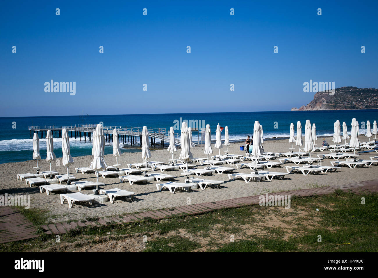 Splendida spiaggia bianca con lettini e ombrelloni con il blu del mare e il molo di Alanya castle rock sullo sfondo Foto Stock