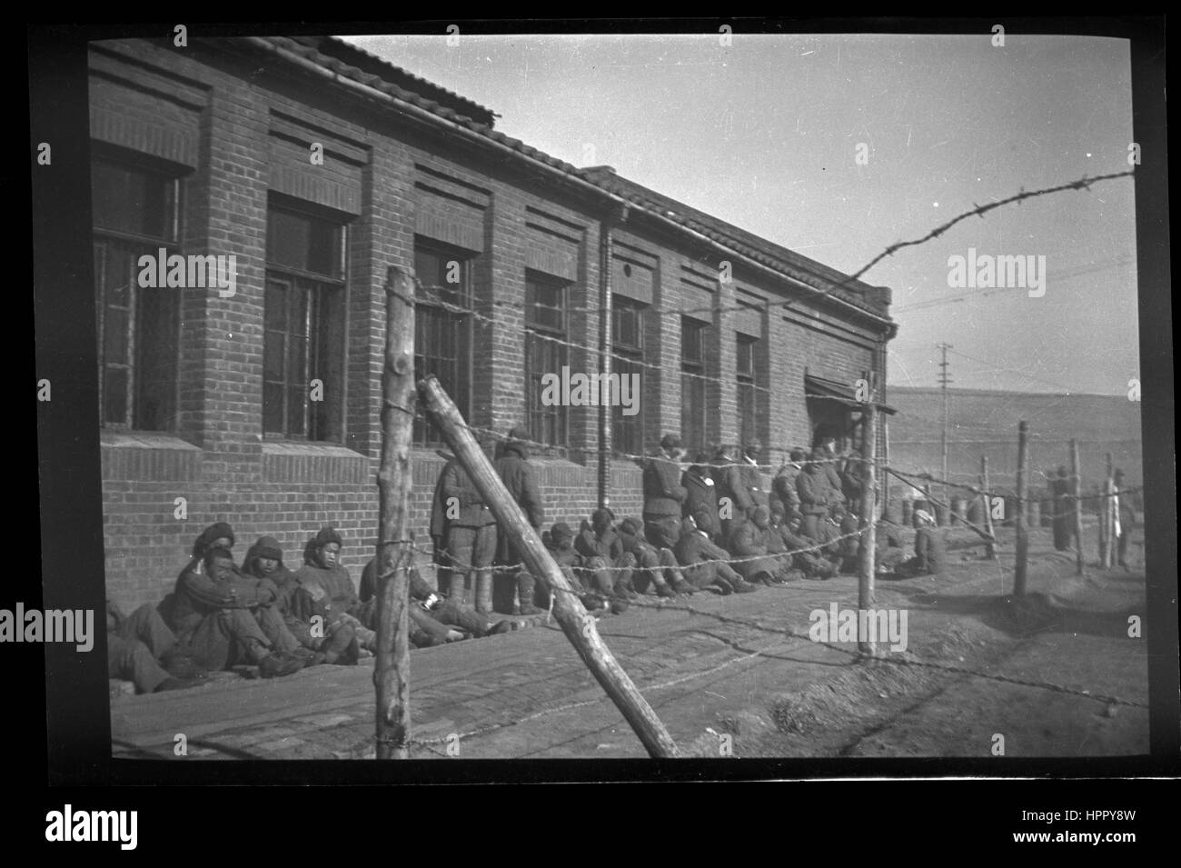Nord coreano POW sit schierate contro un edificio dietro un filo spinato durante la Guerra di Corea. Foto Stock