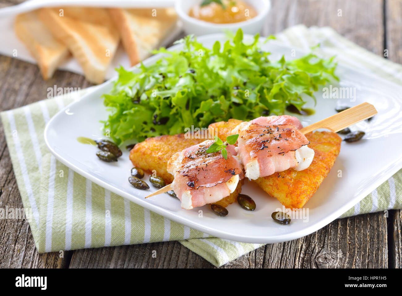 Arrosto di formaggio di capra avvolto in pancetta affumicata e servita su croccante di hash browns fritto con semi di zucca, insalata e la fig la senape Foto Stock