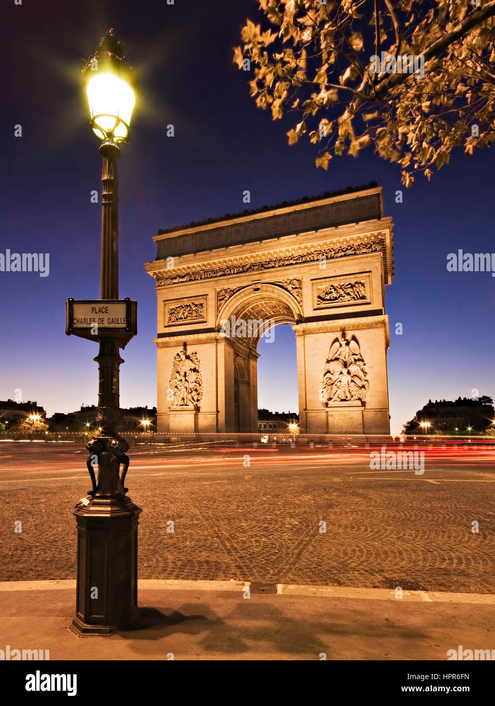 Tempo di notte vista dell'Arc de Triomphe in Parigi Francia. Un lampione è in primo piano con un cartello stradale la lettura Place Charles de Gaulle. Foto Stock