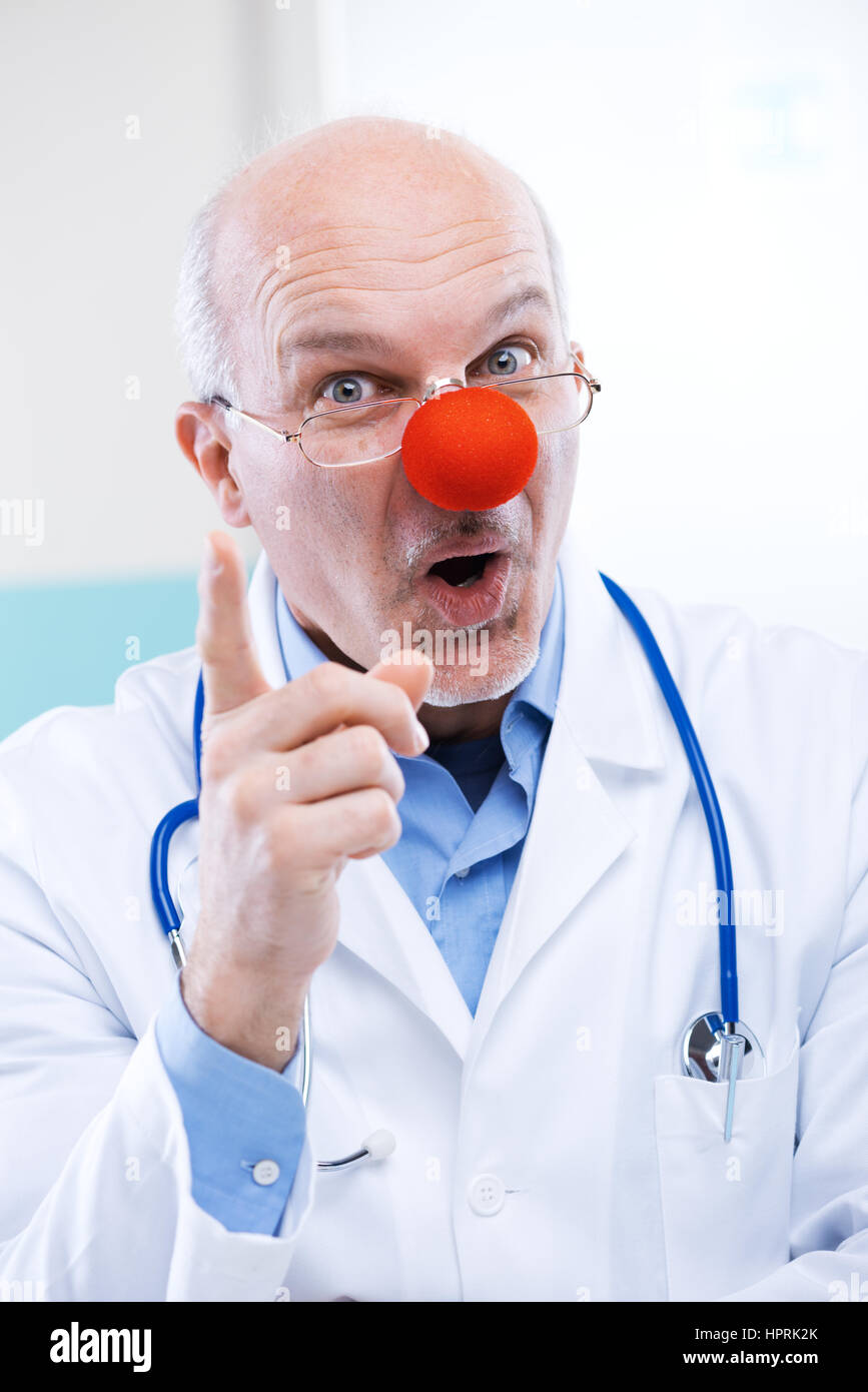 Funny senior medico con red clown naso e espressione divertente. Foto Stock