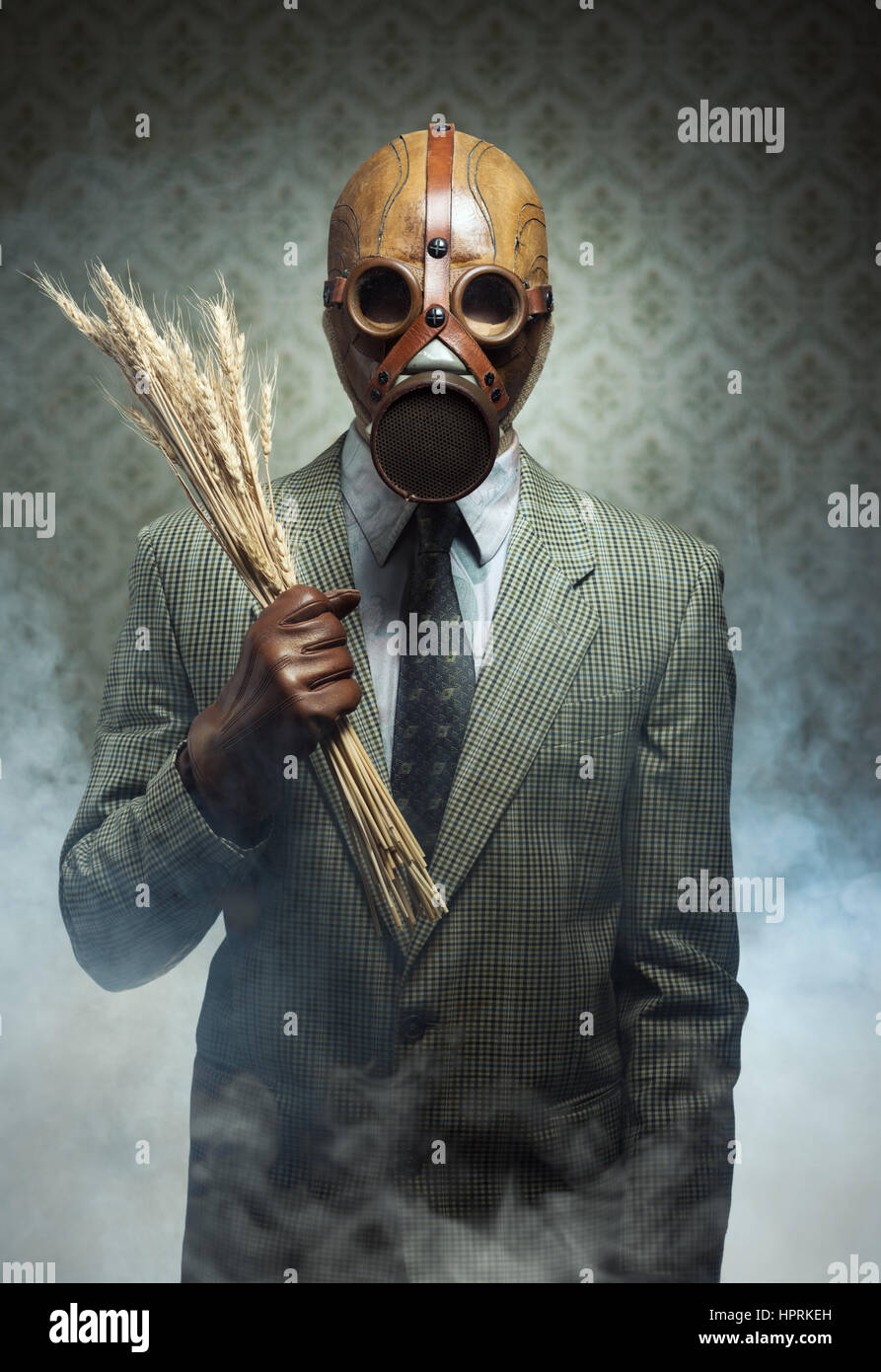 Uomo che indossa una maschera a gas e trattenere spighe di grano con fumo tossico in background. Foto Stock