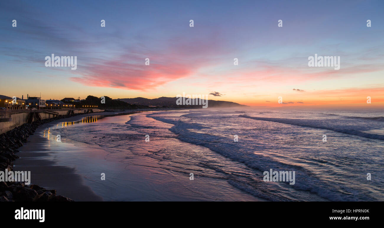 Dunedin, Otago, Nuova Zelanda. Vista sull'Oceano Pacifico su St Clair Beach all'alba, rosa sky riflessa nell'acqua. Foto Stock