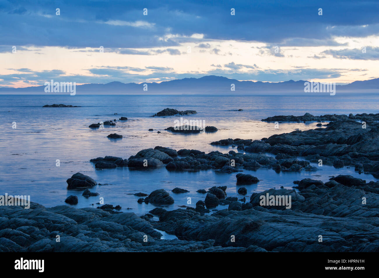 Kaikoura, Canterbury, Nuova Zelanda. Vista su tutta la baia a sud dalla spiaggia rocciosa al crepuscolo. Foto Stock