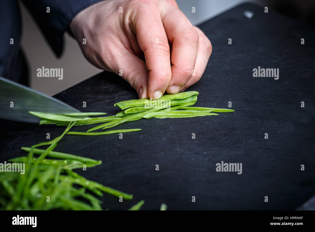 Lo Chef il taglio di pisello verde sul nero tagliere Foto Stock