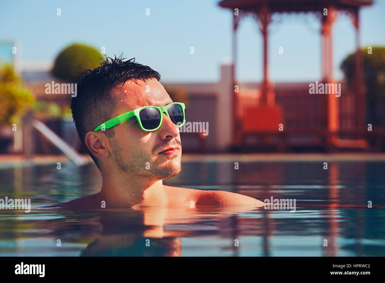 Giovane con occhiali da sole di riposo in piscina durante un giorno d'estate. Foto Stock