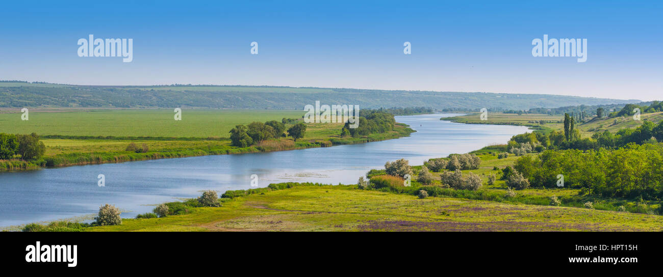 La molla giornata soleggiata sul fiume con il blu del cielo e il verde dei campi Foto Stock
