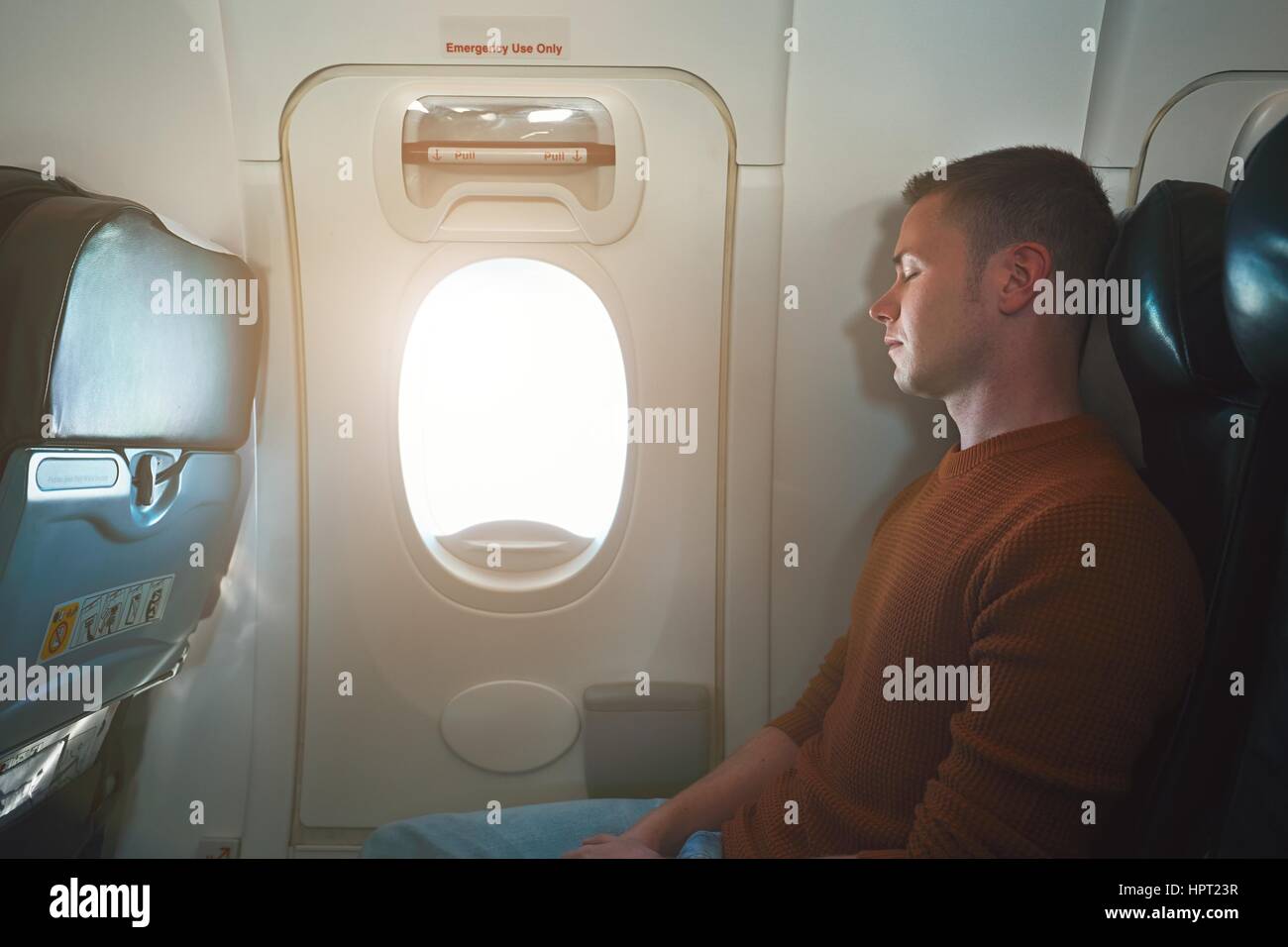 Comodo viaggiare in aereo. Giovane passeggero che dorme sul sedile vicino all'uscita di emergenza dal velivolo. Foto Stock