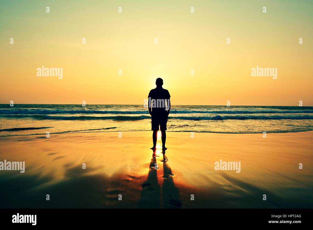 Silhouette di un giovane uomo sulla spiaggia al tramonto. Foto Stock