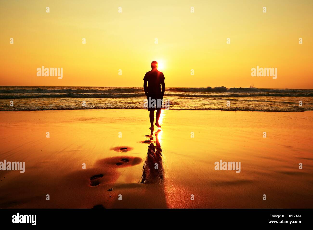 Silhouette di un giovane uomo sulla spiaggia al tramonto. Foto Stock