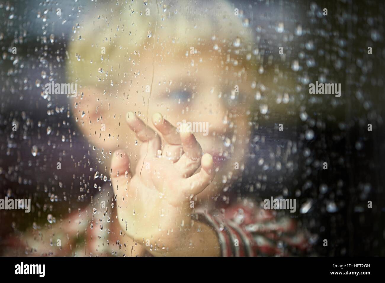 Little Boy dietro la finestra sotto la pioggia - il fuoco selettivo Foto Stock