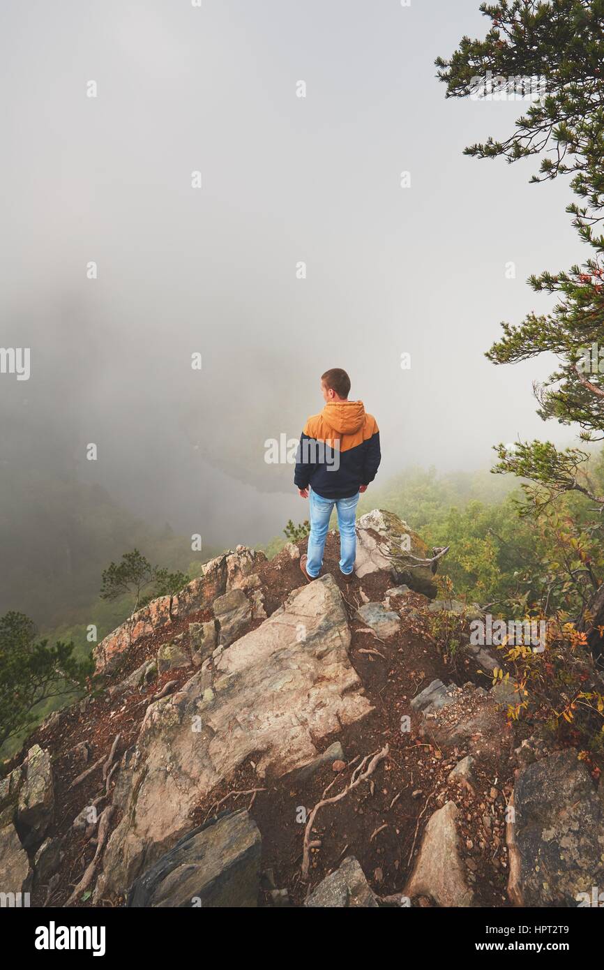 Mattina autunnale. Traveler (escursionista) sulla sommità della roccia sopra la valle del fiume con una fitta nebbia. Foto Stock