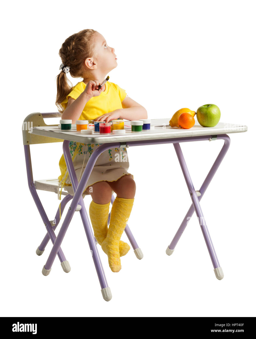 Carino tre-anno ragazza è la pittura con pennello e vernici colorate. Adorabile bambina disegno, seduto dietro il tavolo con frutta fresca e guardando u Foto Stock