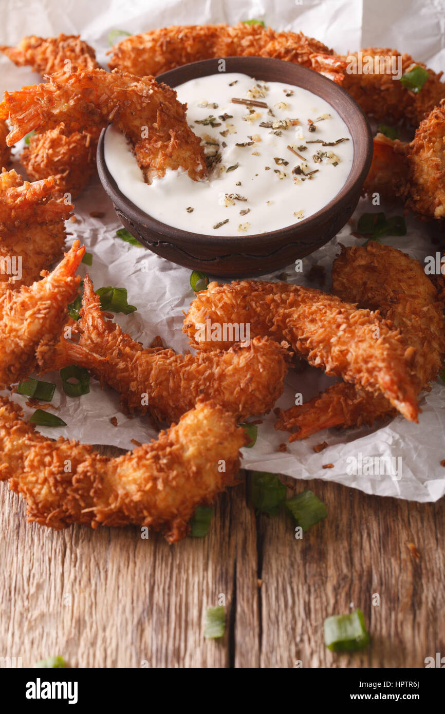 Deliziosi Gamberi fritti in scaglie di cocco close-up e salsa alla panna su pergamena sulla tavola verticale. Foto Stock