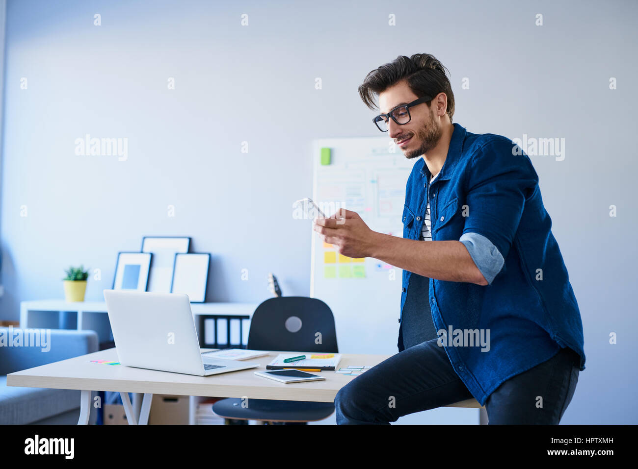 Designer seduto sulla scrivania in ufficio, utilizzando il suo smartphone Foto Stock