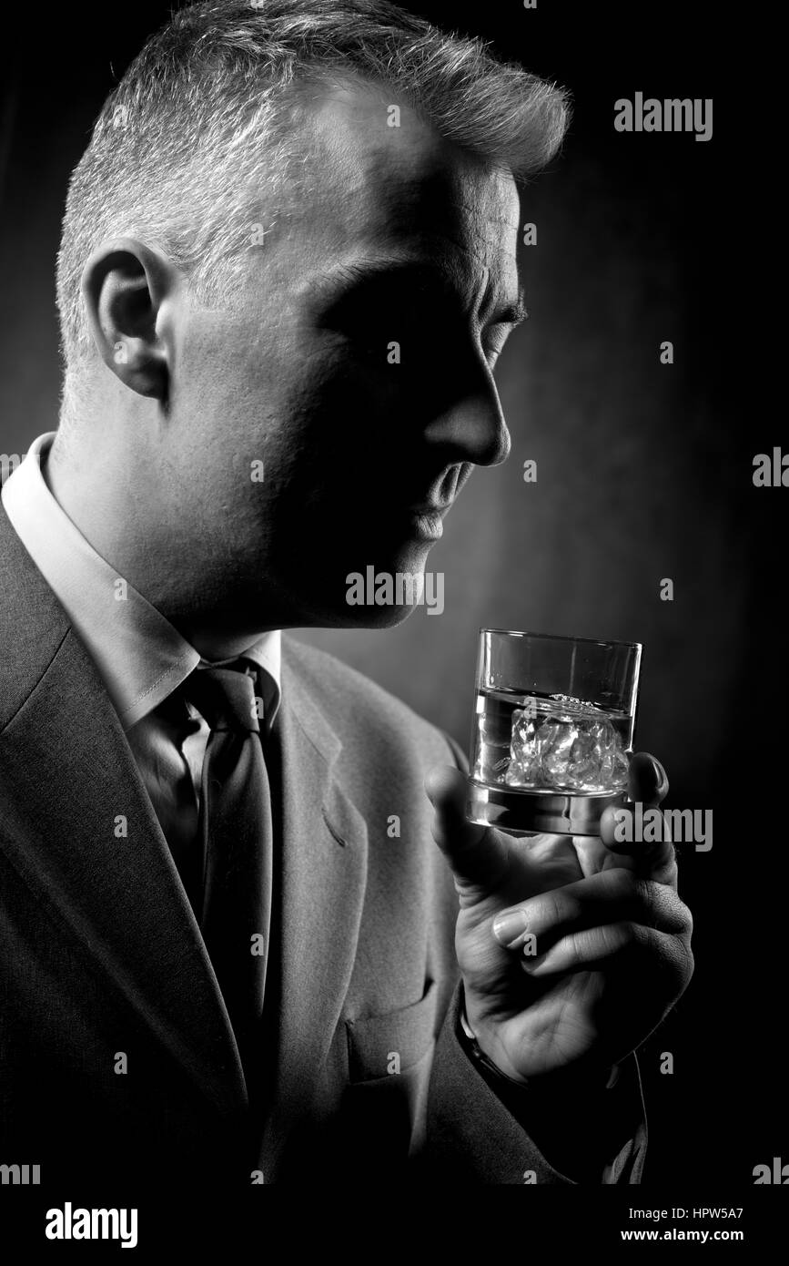 Imprenditore tenendo un bicchiere di whisky su sfondo scuro Foto Stock