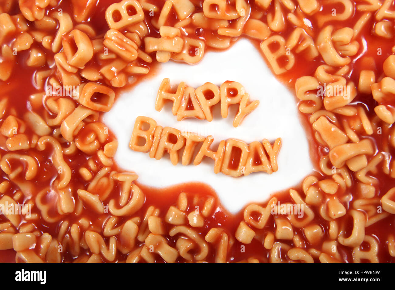 Buon compleanno scritto in spaghetti lettere circondato con lettere illeggibili. Foto Stock