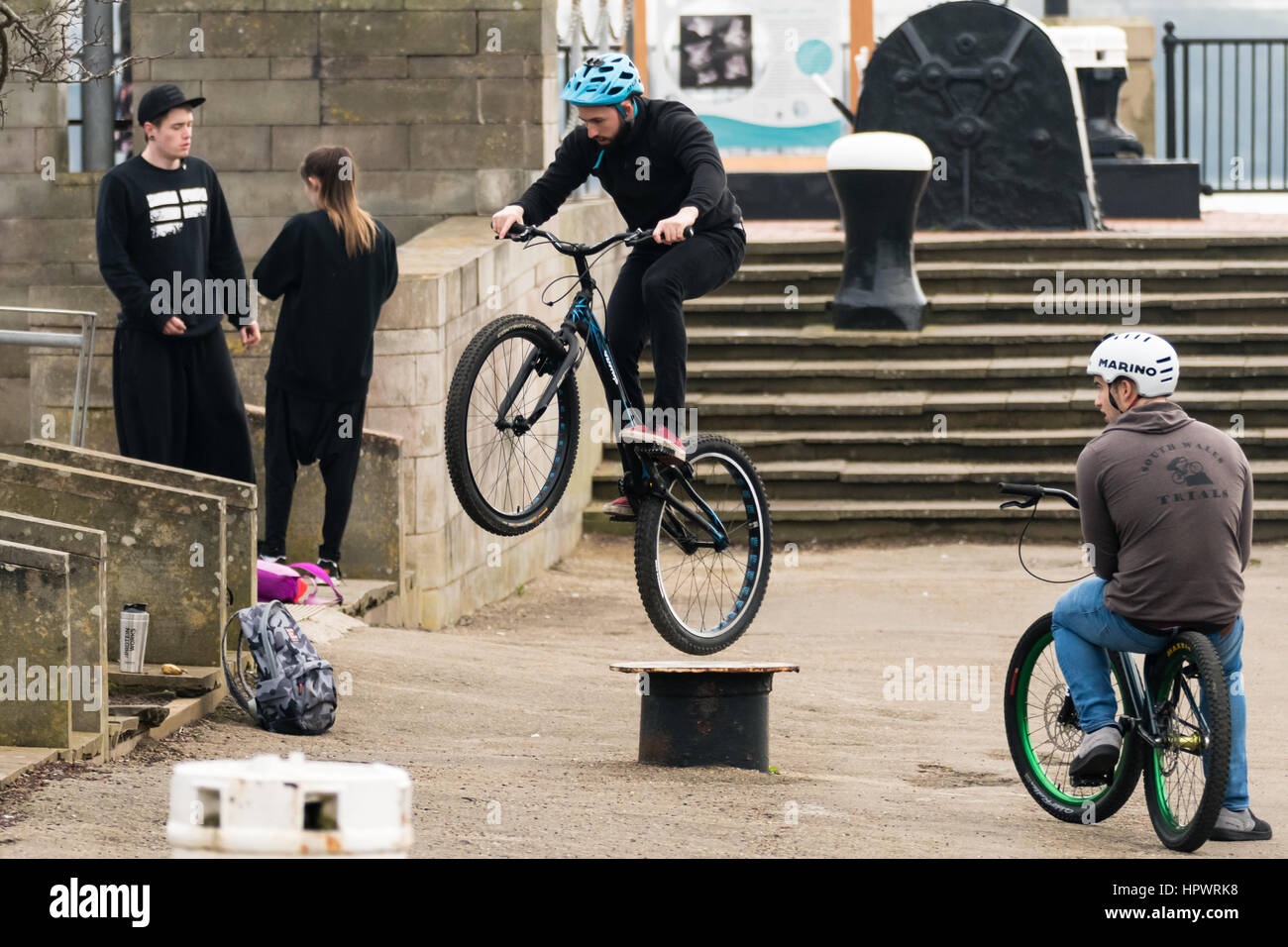Cardiff Wales, Regno Unito - 18 Febbraio 2017: Bici piloti di eseguire trucchi su arredo urbano. Giovani uomini fanno salti di divertimento con gli amici intorno permanente Foto Stock