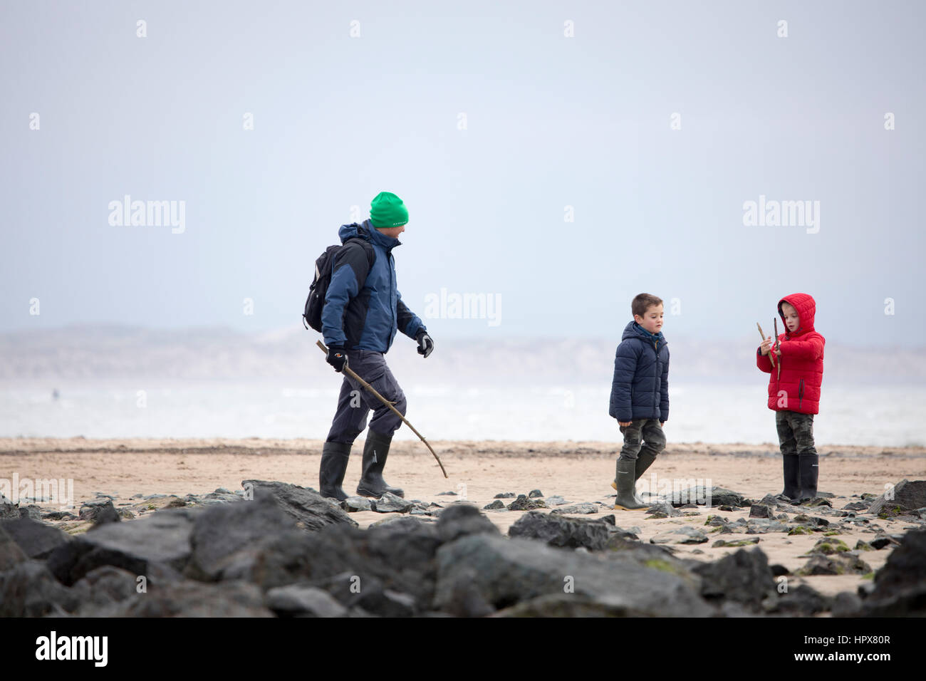 La famiglia include il padre e i due figli godendo di una passeggiata sulla spiaggia in inverno sulla spiaggia di Newborough sull'Isola di Anglesey, Galles, Regno Unito Foto Stock