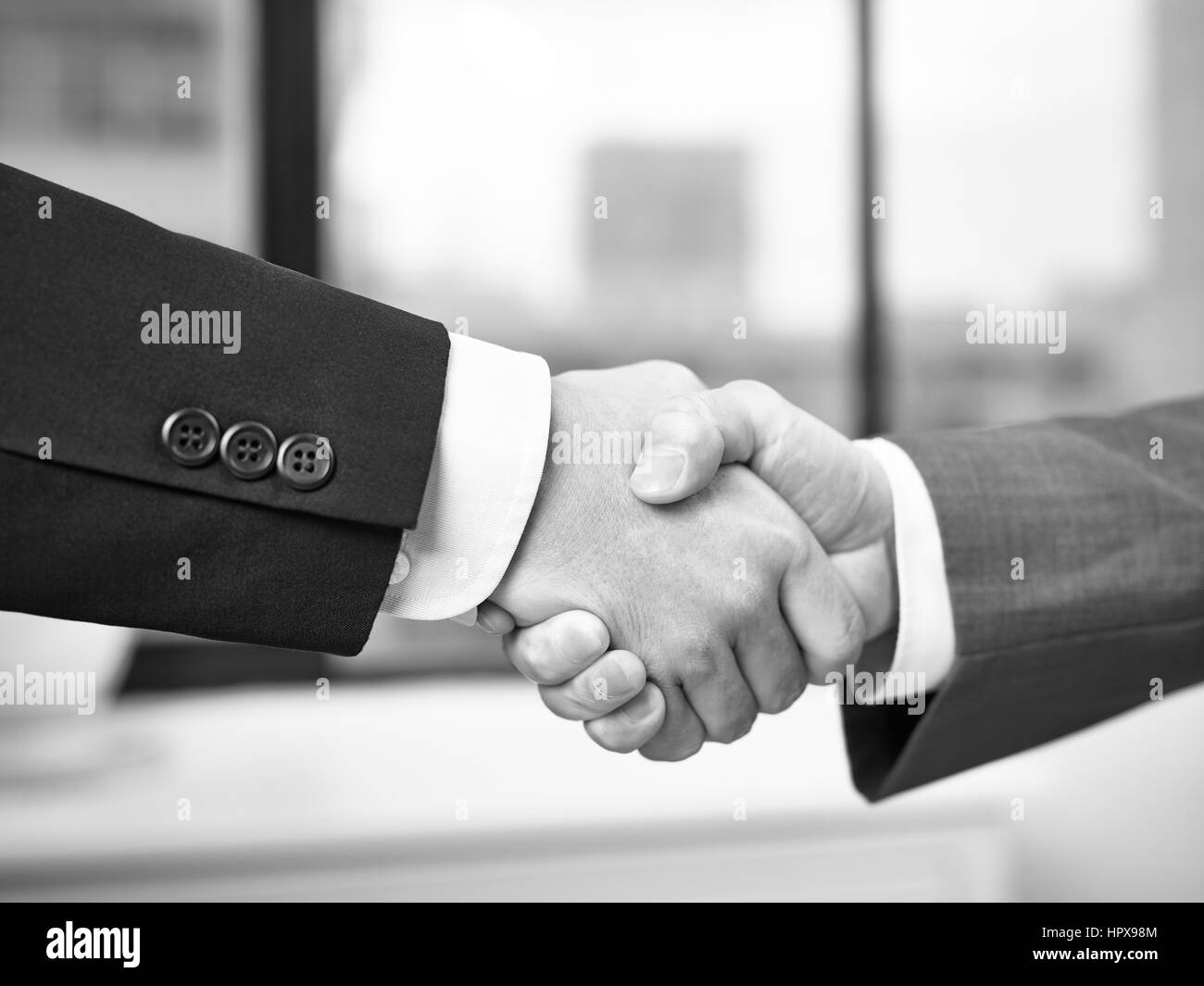 Due uomini di affari aziendali stringono le mani in ufficio, in bianco e nero. Foto Stock