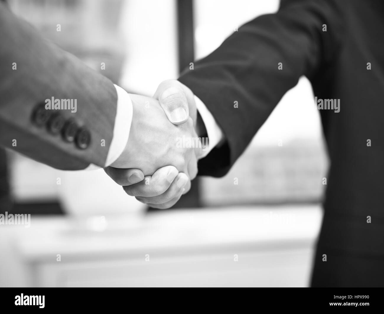 Due uomini di affari aziendali stringono le mani in ufficio, in bianco e nero. Foto Stock