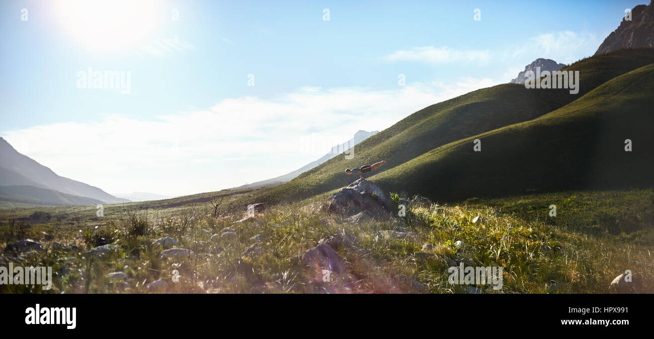 Giovane uomo facendo handstand orizzontale su roccia nella soleggiata valle remota Foto Stock