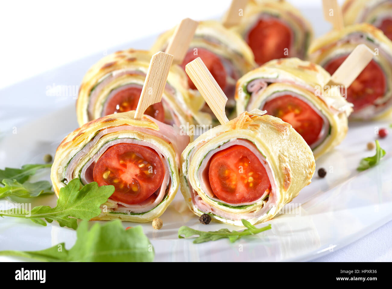 Deliziosi stuzzichini: rotoli di frittelle sottili (crepes) con prosciutto, formaggio spalmabile, insalata di rucola e pomodorini Foto Stock