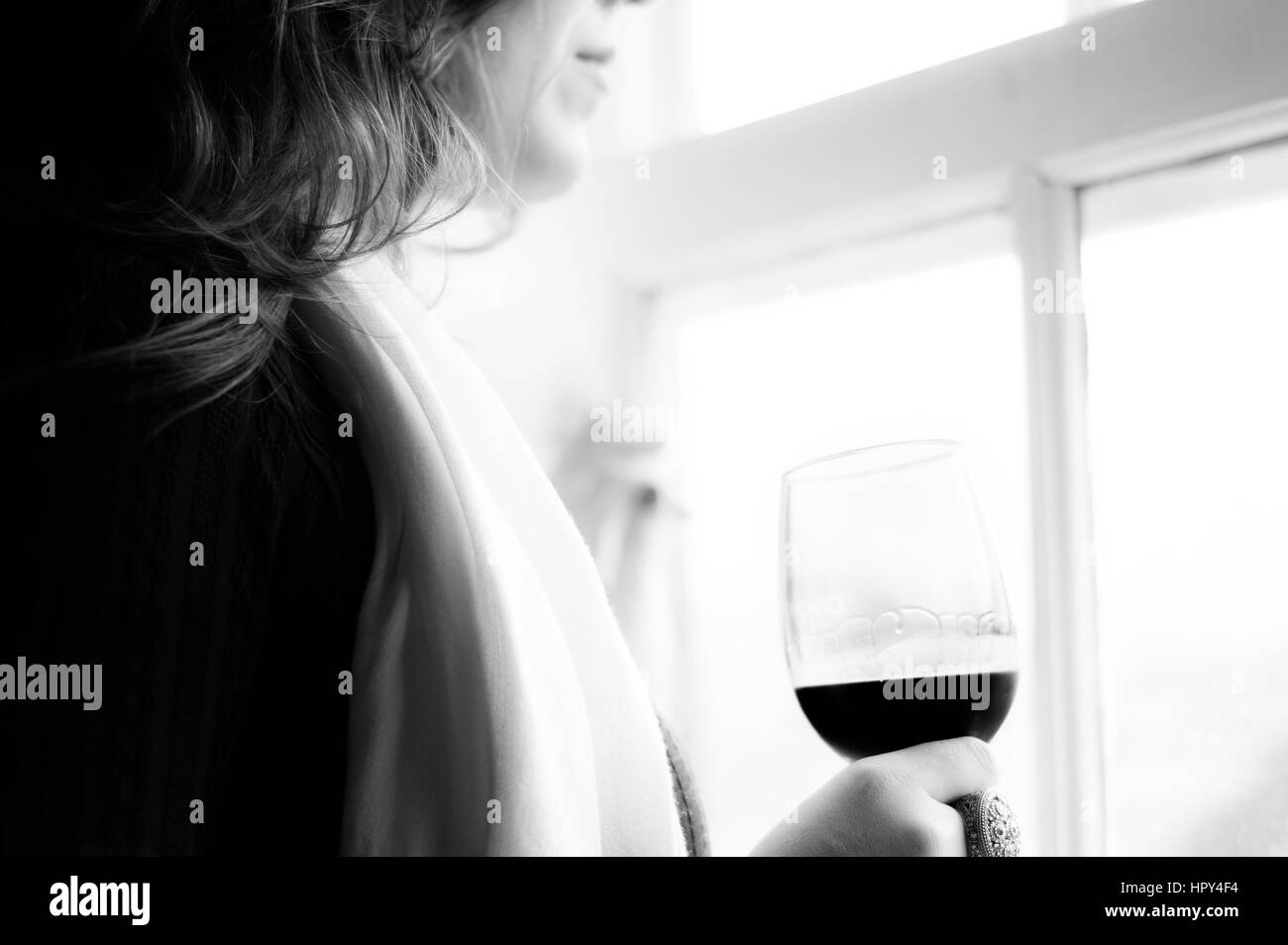 Un elegante donna in piedi da una finestra con in mano un bicchiere di vino rosso. Foto Stock