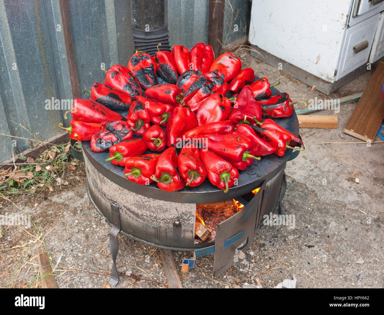 Peperoni rossi tostatura su un legno-sparò stufa in preparazione per la realizzazione di ajvar, un tradizionale piatto macedone. Foto Stock