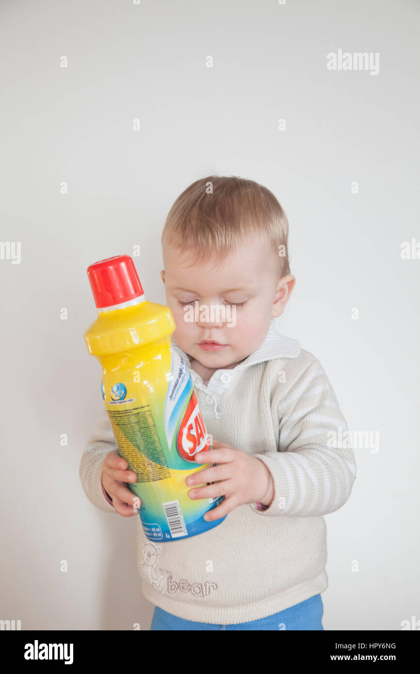 Piccolo bambino che gioca con i prodotti di pulizia a casa su sfondo bianco Foto Stock