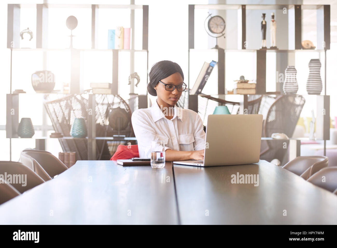 Attraente giovane professionista ben educati nero donna occupata la digitazione sul proprio portatile mentre si è seduti al suo tavolo da pranzo a casa con un display di grandi dimensioni Foto Stock