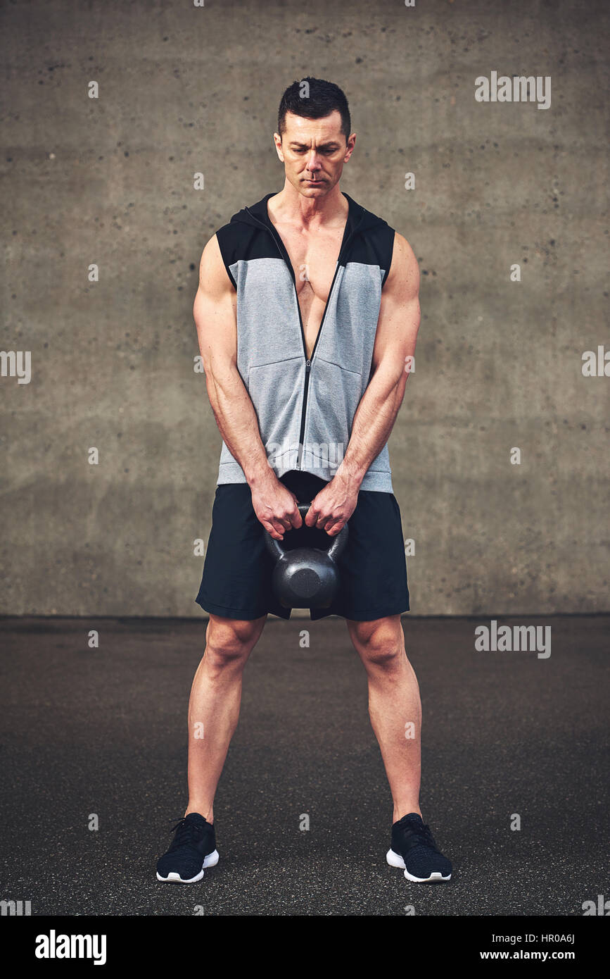 Giovane uomo forte in azienda di abbigliamento sportswear kettlebell pesanti su sullo sfondo di un muro di cemento. Foto Stock
