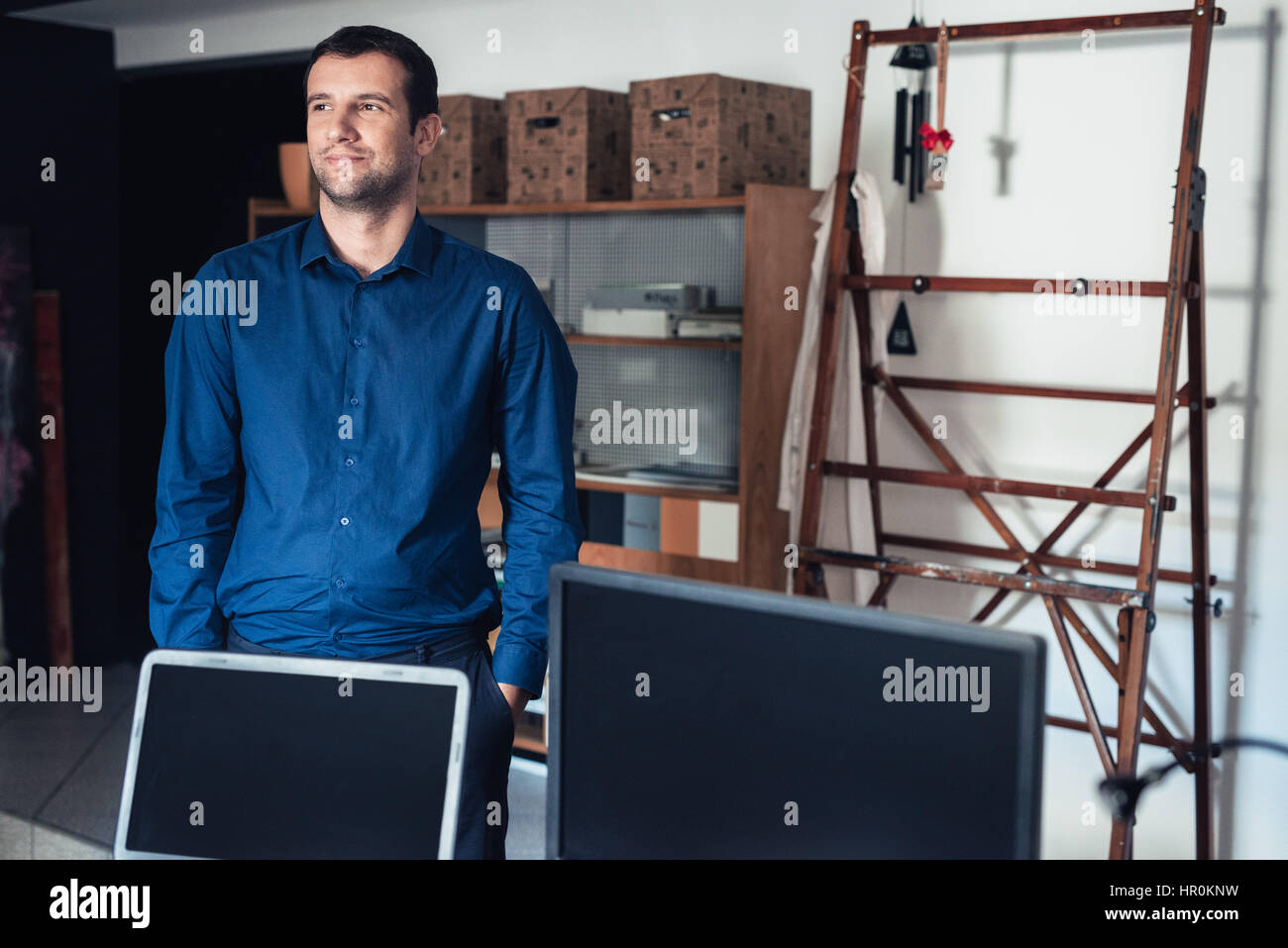 Fiducioso e di successo di giovane imprenditore a guardare in profondità nel pensiero mentre in piedi con le mani in tasca in un grande lavoro di studio Foto Stock