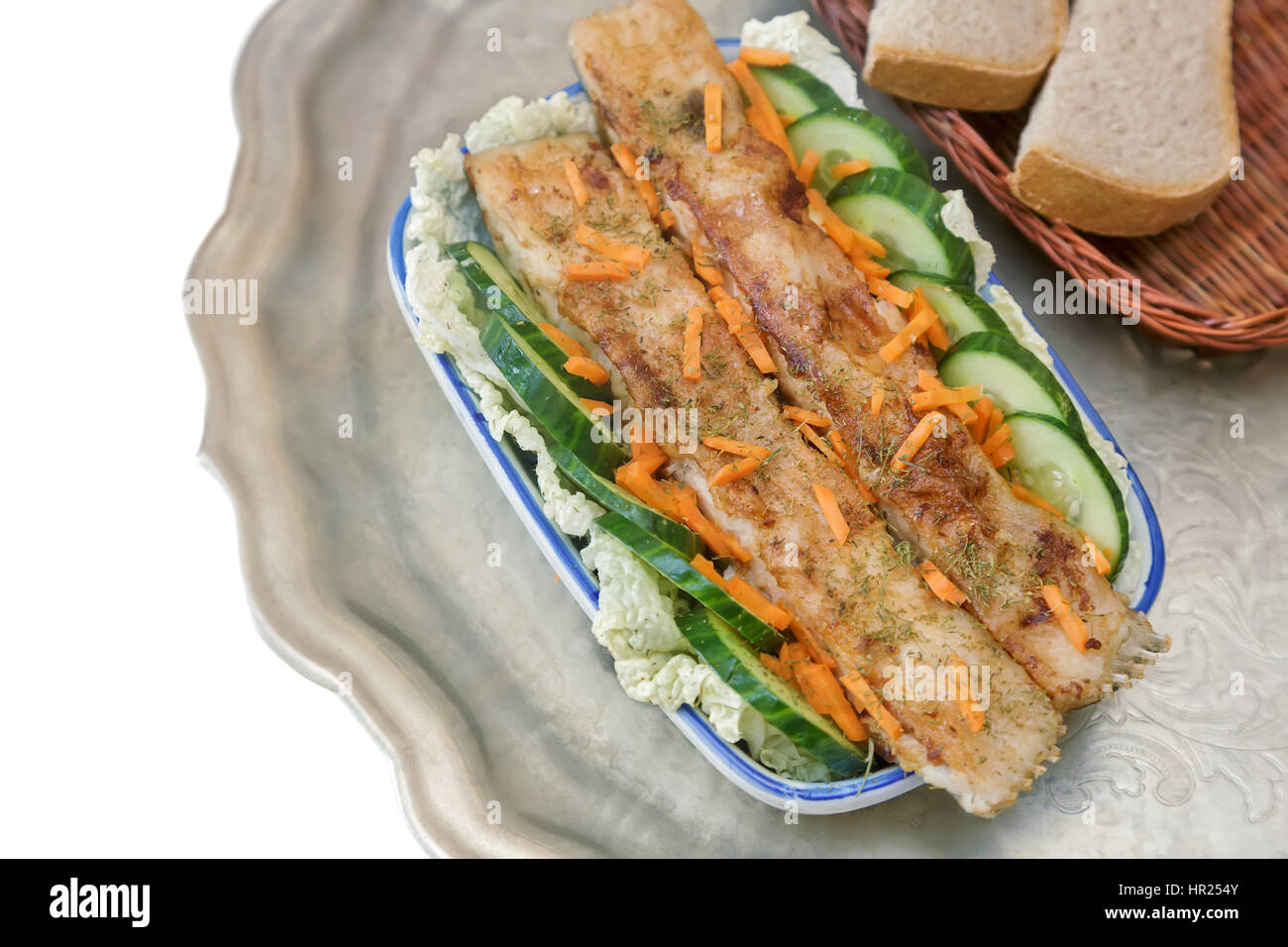 In un piatto di ceramica sul tavolo il pesce fritto con lattuga e cetriolo.  Piatti a base di pesce è su un vassoio di metallo Foto stock - Alamy