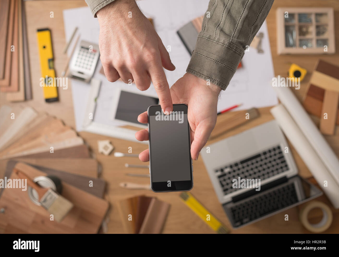 Home decorator le mani tenendo un touch screen mobile phone, desktop con strumenti, laptop e campioni di legno su sfondo, vista dall'alto Foto Stock