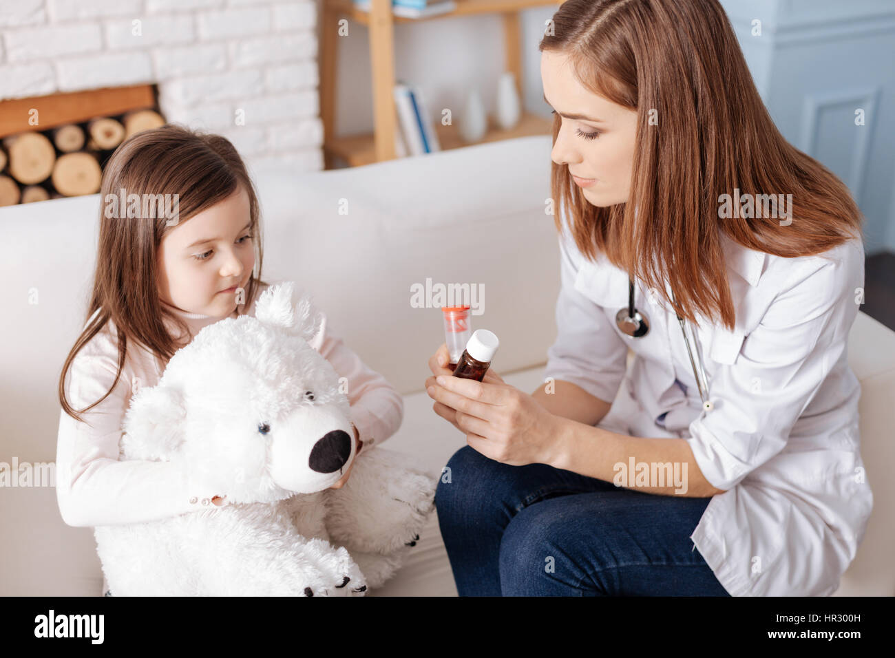 Ogni vostra giornata norm. Piacevole professionale medico tenendo pillole mentre dà suggerimenti alla bambina che è seduto con il suo giocattolo soffici Foto Stock