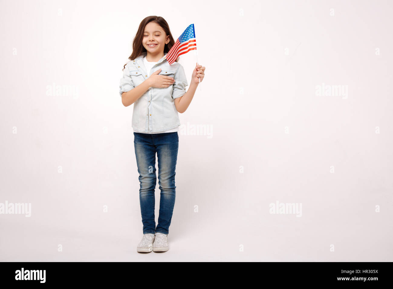 Onorando la mia nazione. Allegro vivace bambina tenendo la bandiera americana e toccando il suo torace pur esprimendo felicità Foto Stock