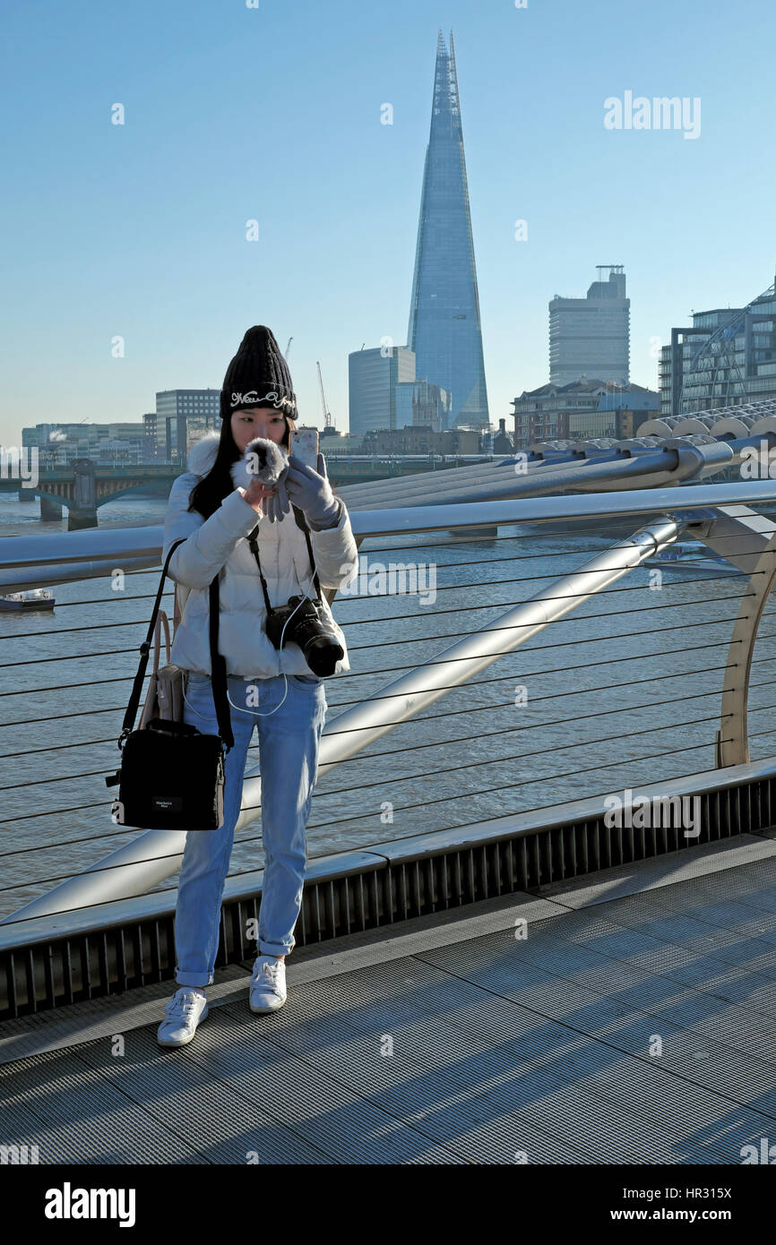 Giovane donna prendendo un selfie su una soleggiata giornata invernale e sul Millennium Bridge & vista della Shard edificio nel sud di Londra Inghilterra REGNO UNITO KATHY DEWITT Foto Stock