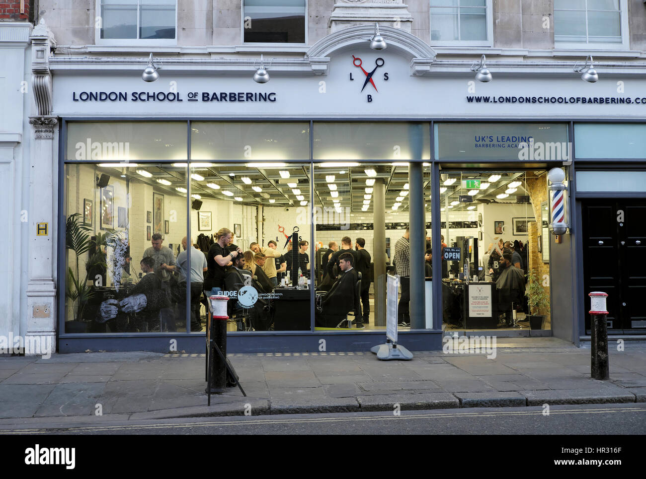 Vista esterna dell'interno London School of Barbering shop con apprendisti il taglio di capelli di clienti di Smithfield, Londra KATHY DEWITT Foto Stock