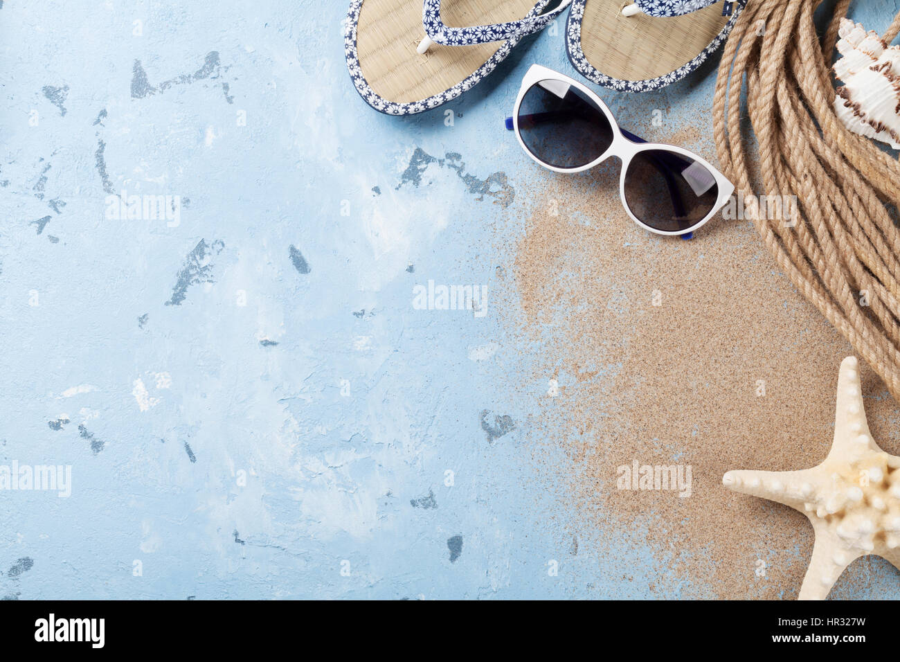 Accessori da spiaggia. Occhiali da sole, flip-flop e conchiglie di mare su sfondo di pietra. Vista da sopra con lo spazio di copia Foto Stock
