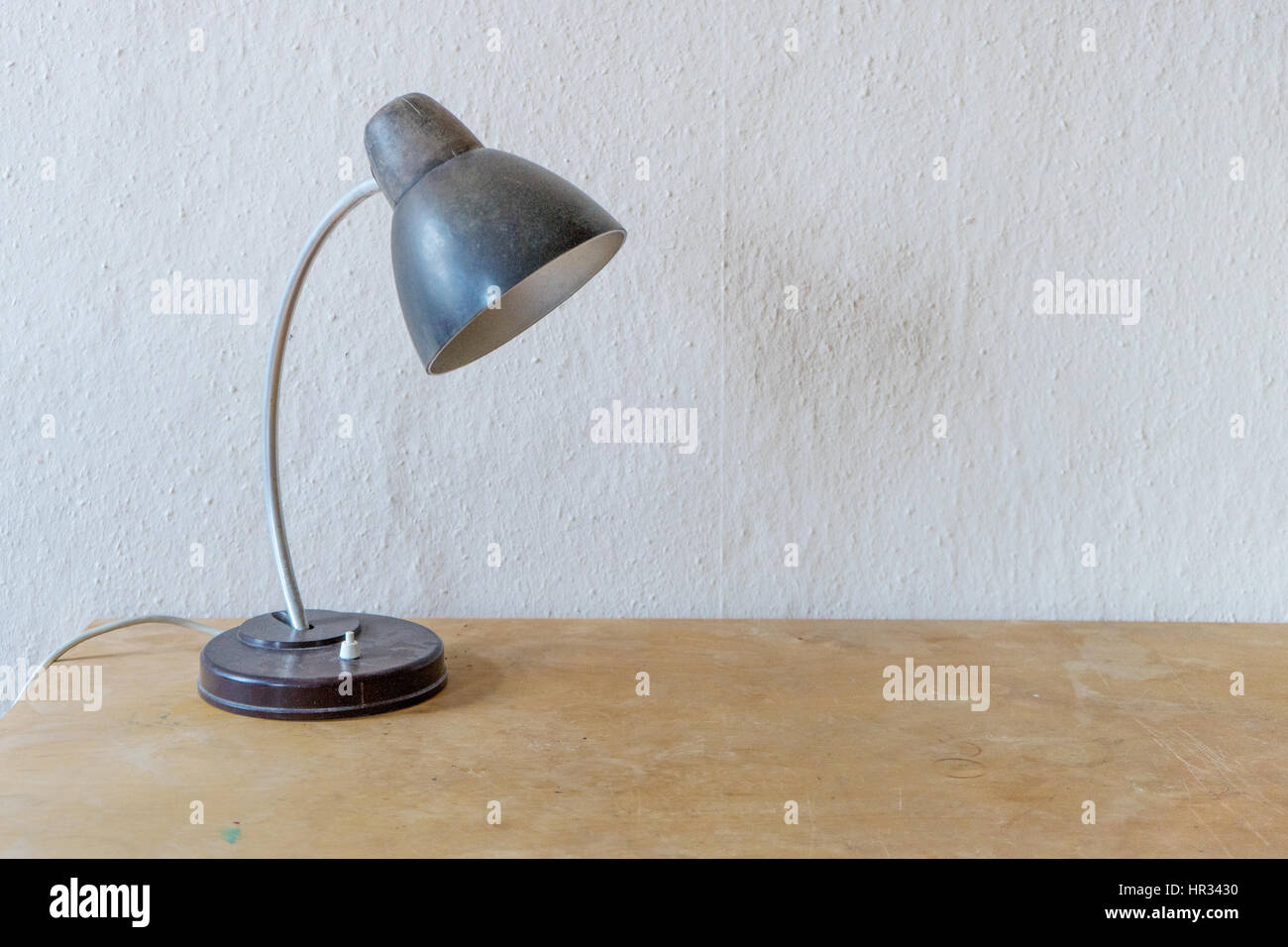 Vecchia lampada da tavolo su una tavola di legno di fronte un muro bianco Foto Stock