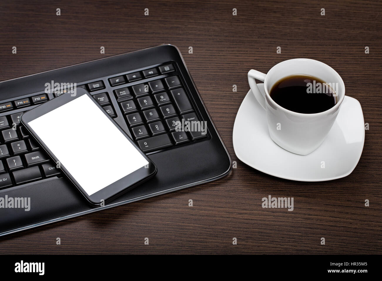 Moderno smartphone con schermo vuoto, la tastiera del computer e la tazza di caffè in legno scuro, scrivania in ufficio. Foto Stock