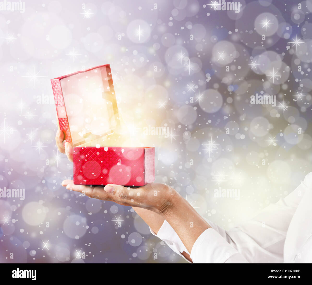 Mani e pening una confezione regalo rossa con magici effetti speciali luci. Foto Stock