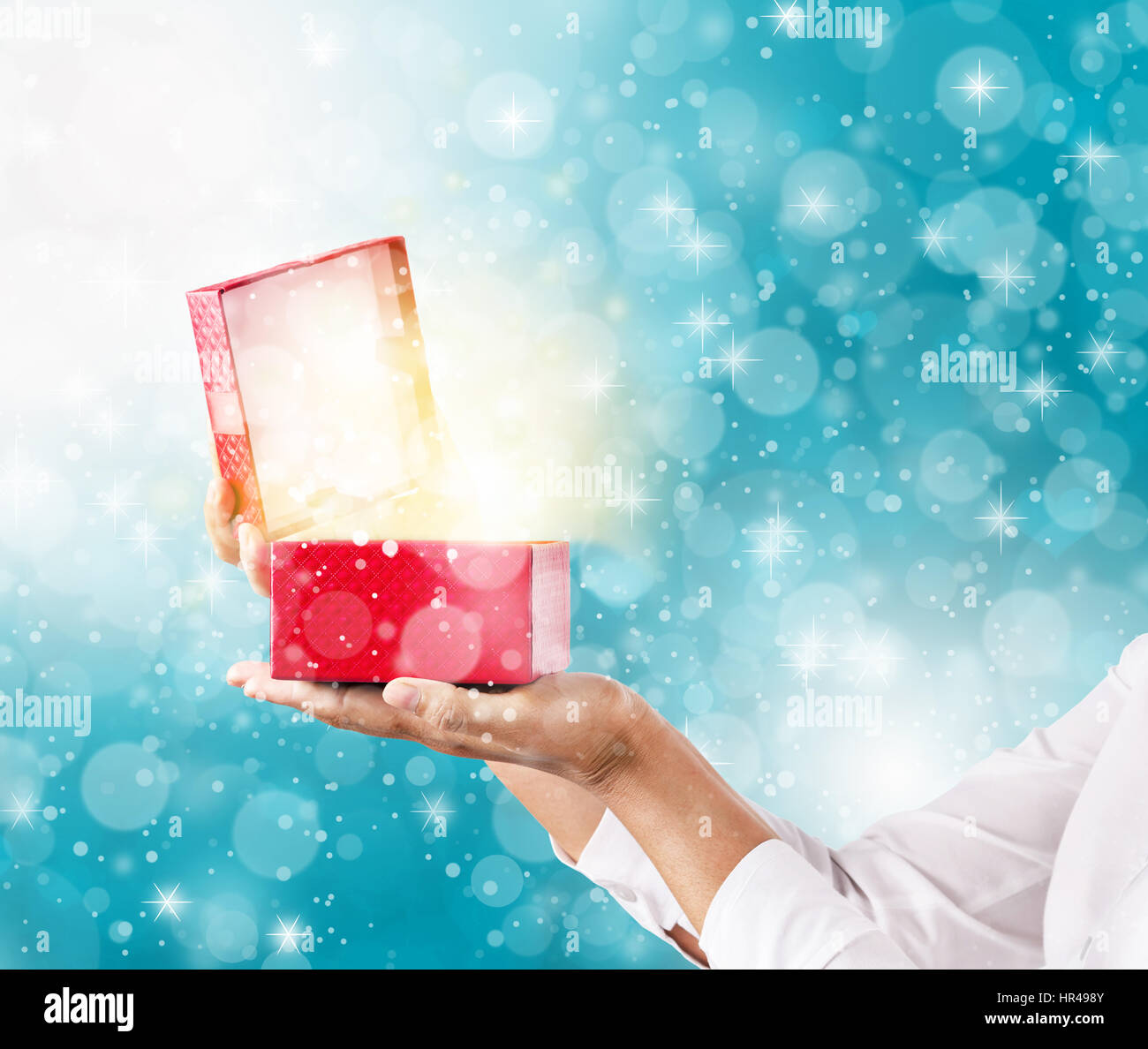 Mani e pening una confezione regalo rossa con magici effetti speciali luci. Foto Stock