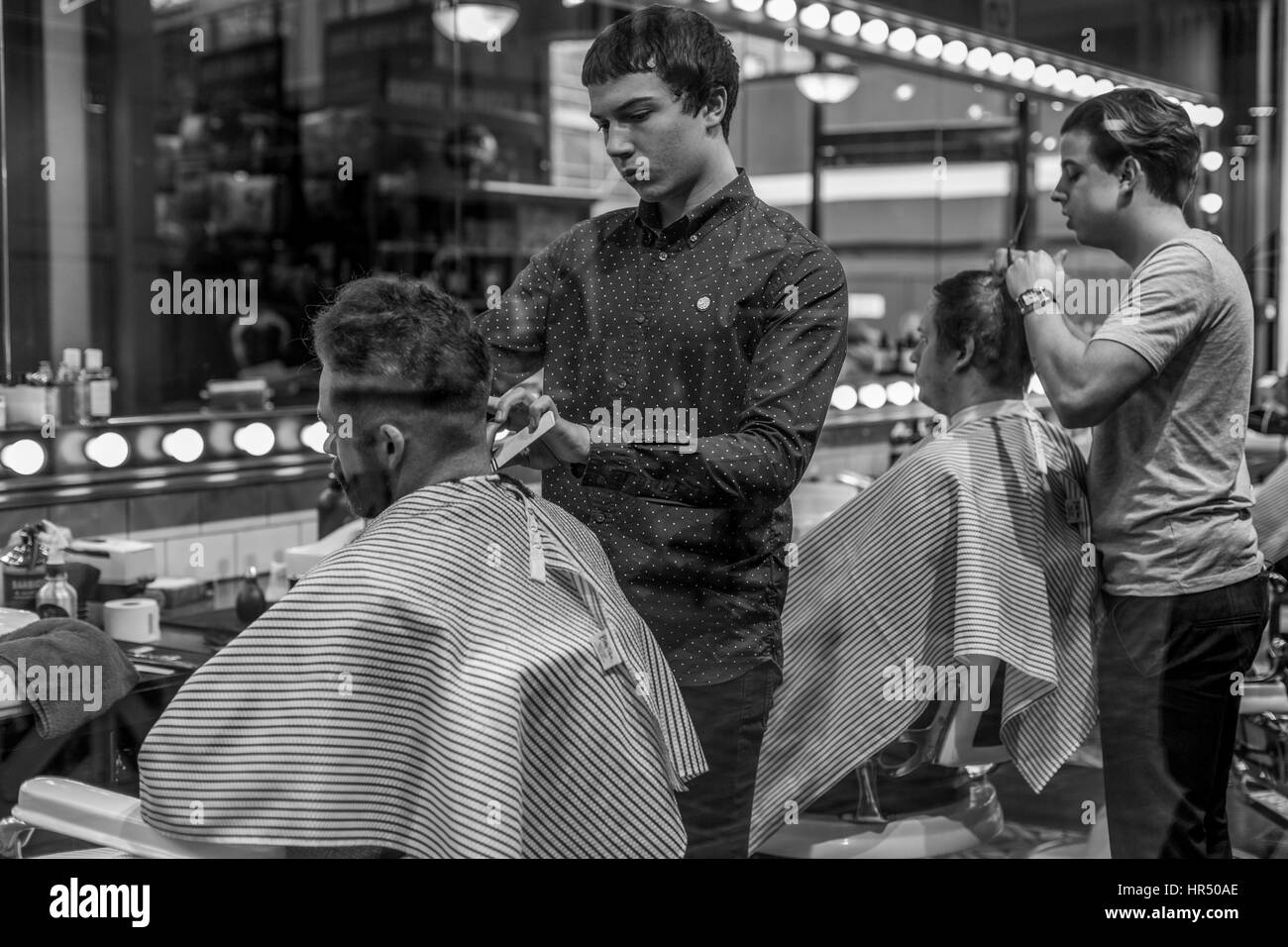 Due giovani uomini che hanno i loro capelli tagliati, in un negozio alla moda Old Spitalfields Market barber, Londra, Inghilterra , Regno Unito Foto Stock