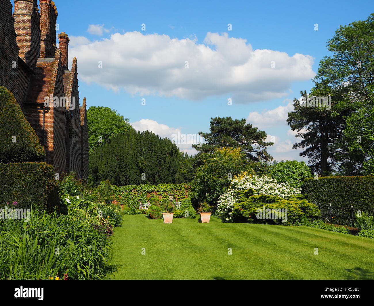 Sud ovest giardino a Chenies Manor House con camini, prato a strisce, fiore di confine e cielo blu con soffici nuvole bianche. Foto Stock