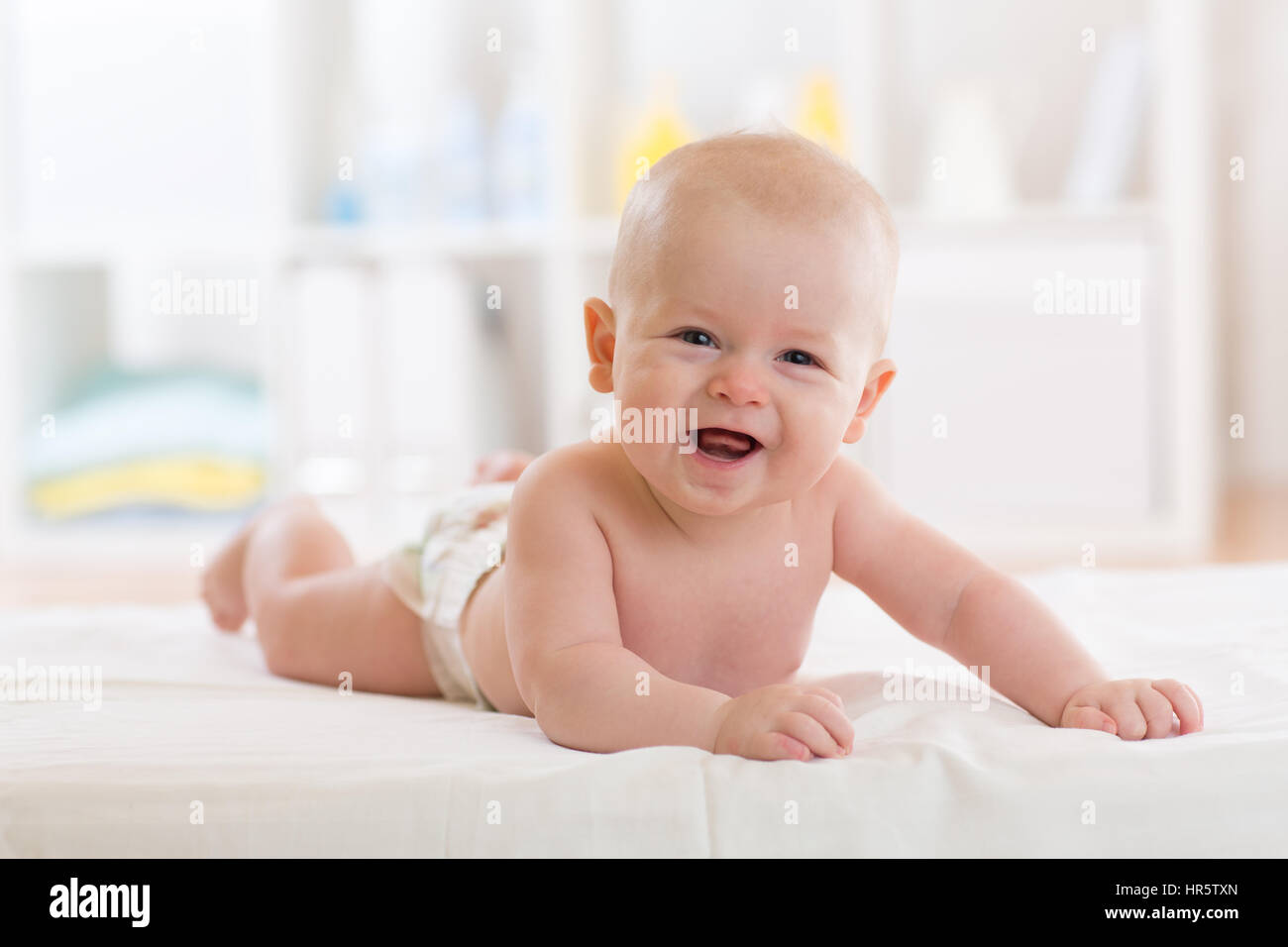 Neonato ragazzo indossa pannolino giacenti nel letto in bianco e luminosa camera da letto o il vivaio. Prodotti tessili e biancheria da letto per i bambini Foto Stock