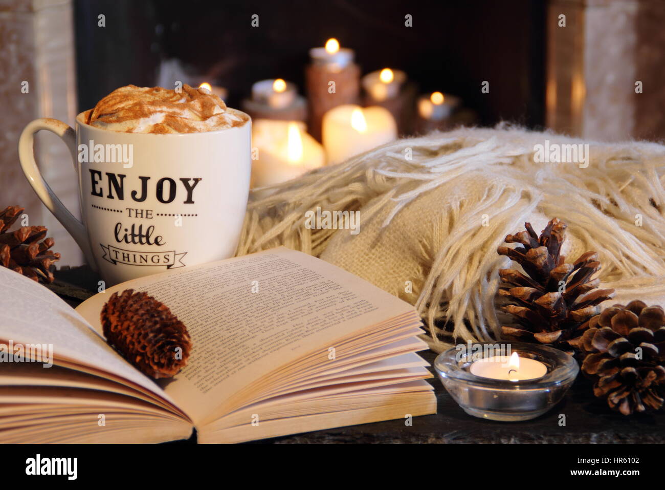 La lettura a lume di candela con un caminetto aperto in un accogliente English home con una tazza di caffè cremoso e una coperta (tiro) su una sera d'inverno Foto Stock