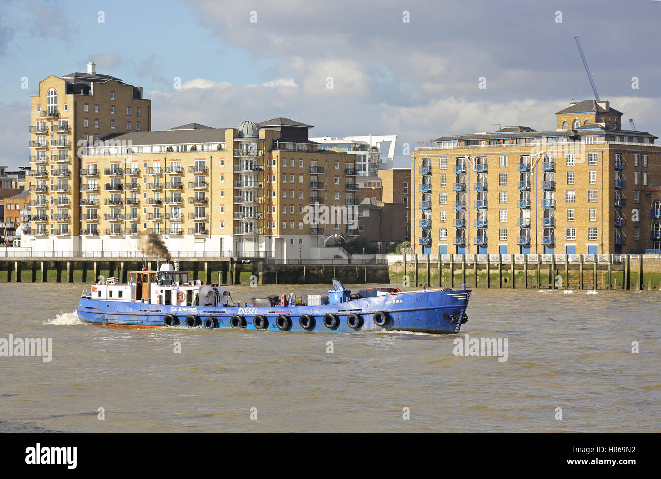 Un piccolo diesel vele di navi cisterna a valle sul fiume Tamigi a Londra, passando moderni loft appartamenti in stile Wapping Foto Stock