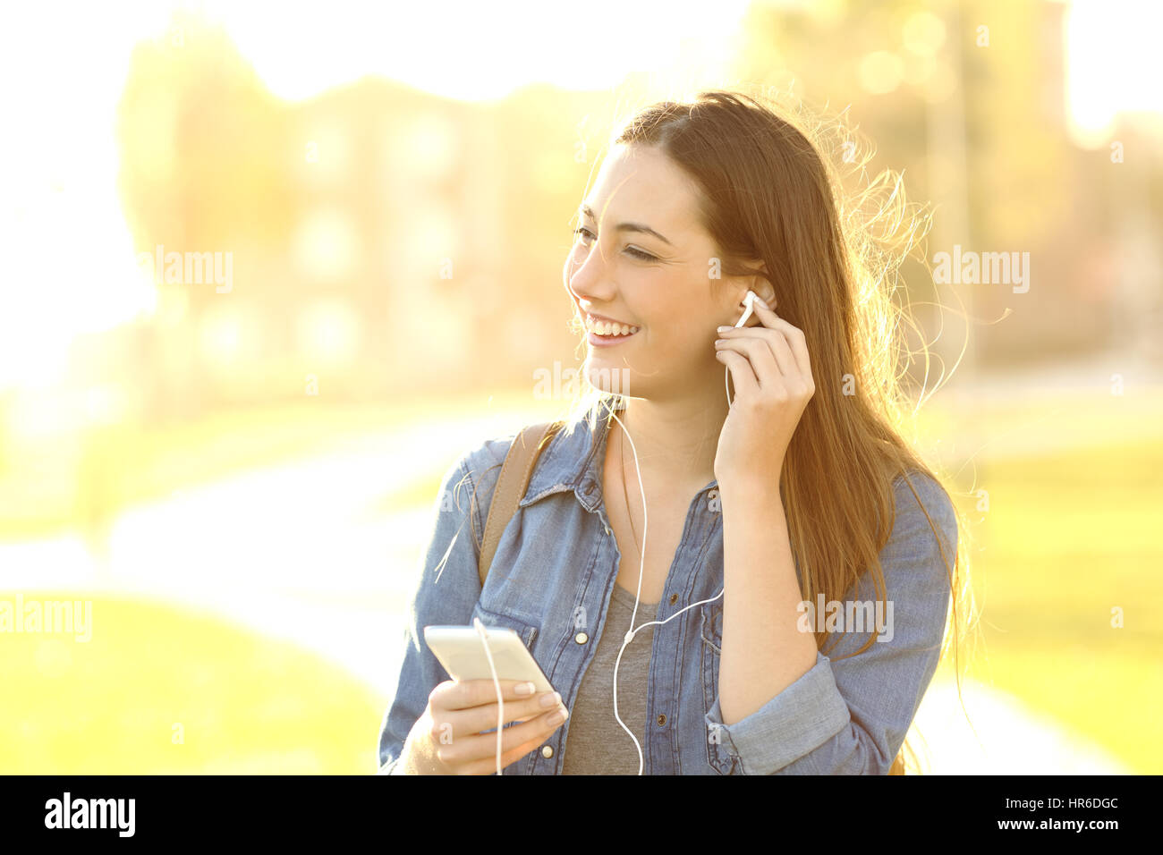 Una donna in ascolto di musica con cuffie in strada al tramonto con una luce calda in background Foto Stock
